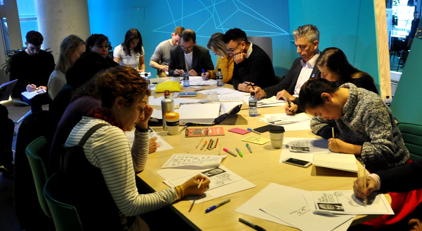 A large group sitting at one large table, drawing.