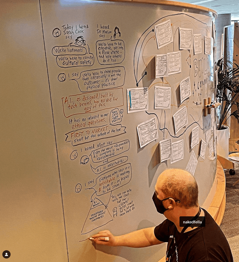 David, a man in a t-shirt and a black mask, at a whiteboard sketchnoting.